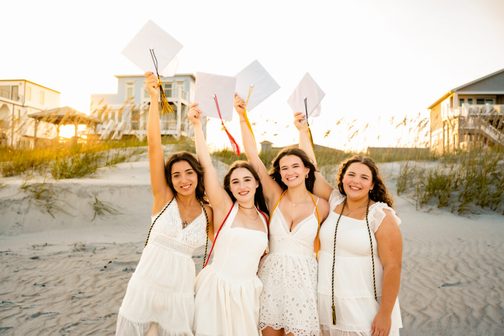 four girlfriends standing on the beach with a graduation cap and tassels