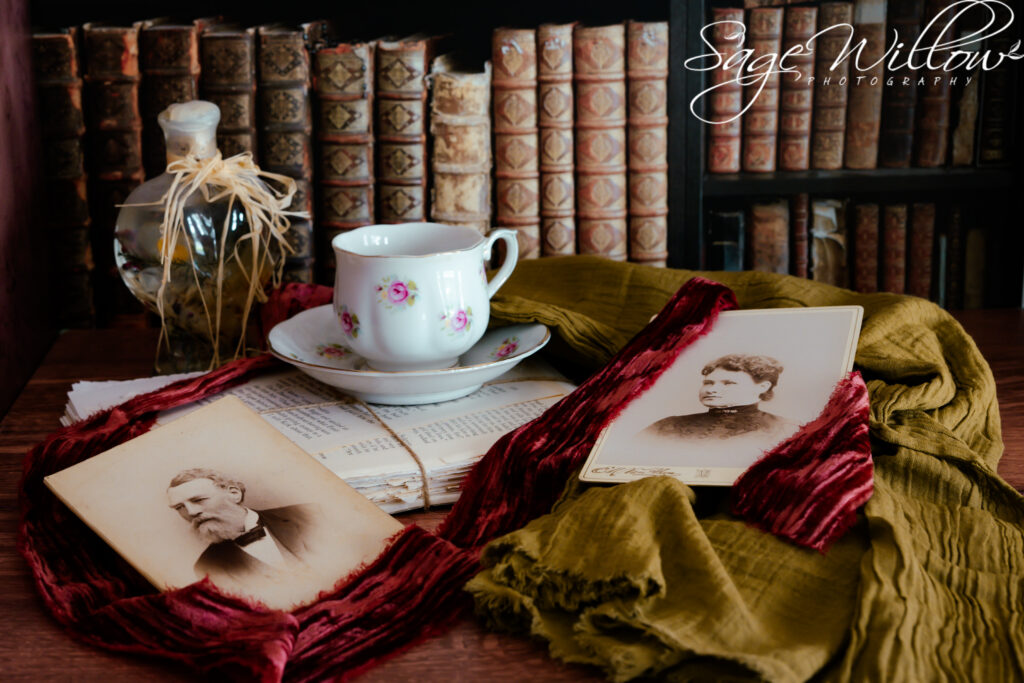 Old photos of a man and woman laying on a table with a tea cup and books behind the table.
