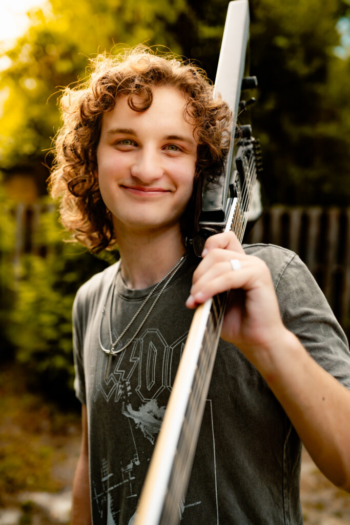 color photo of a young man standing outside with a guitar over his shoulder