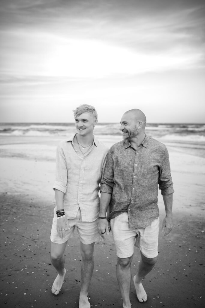 black and white photo of a father and his adult son walking and smiling on the beach