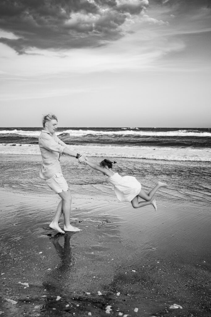 Black and white photo of an uncle swinging his niece around on the beach.