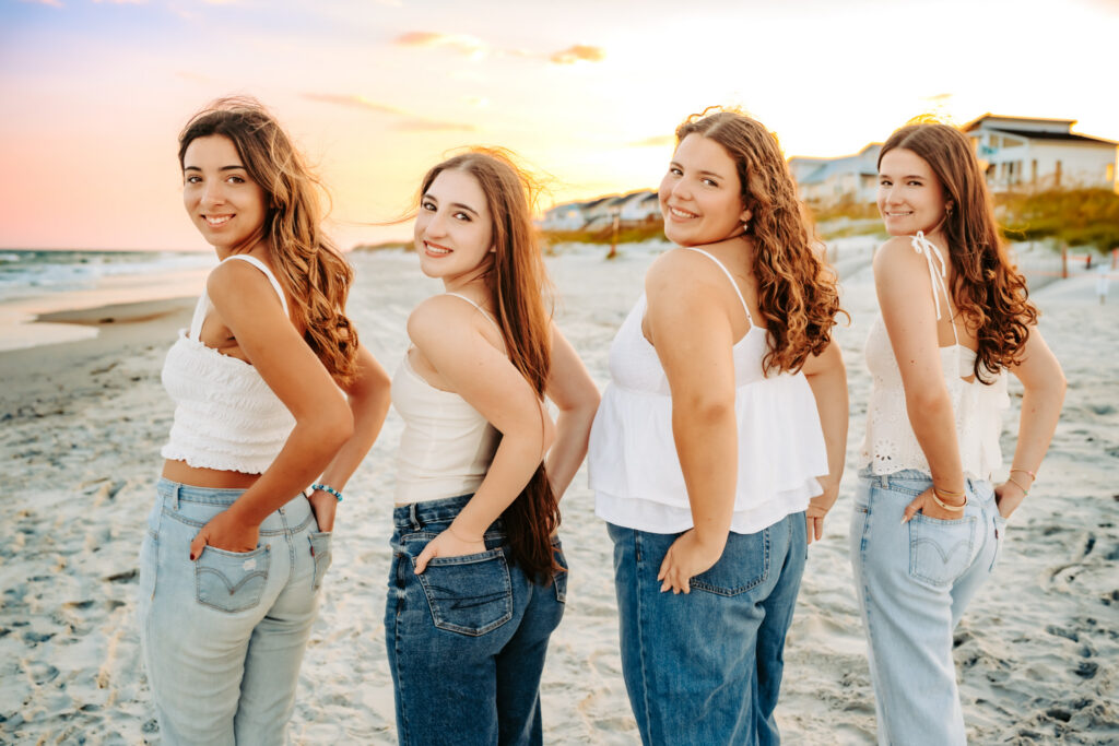 four girlfriends looking over their shoulders as they walk along the beach