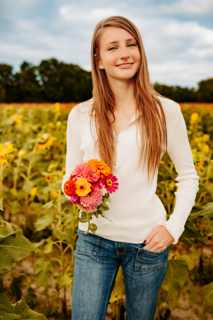 high school senior girl standing in a flower field with flowers, smiling.