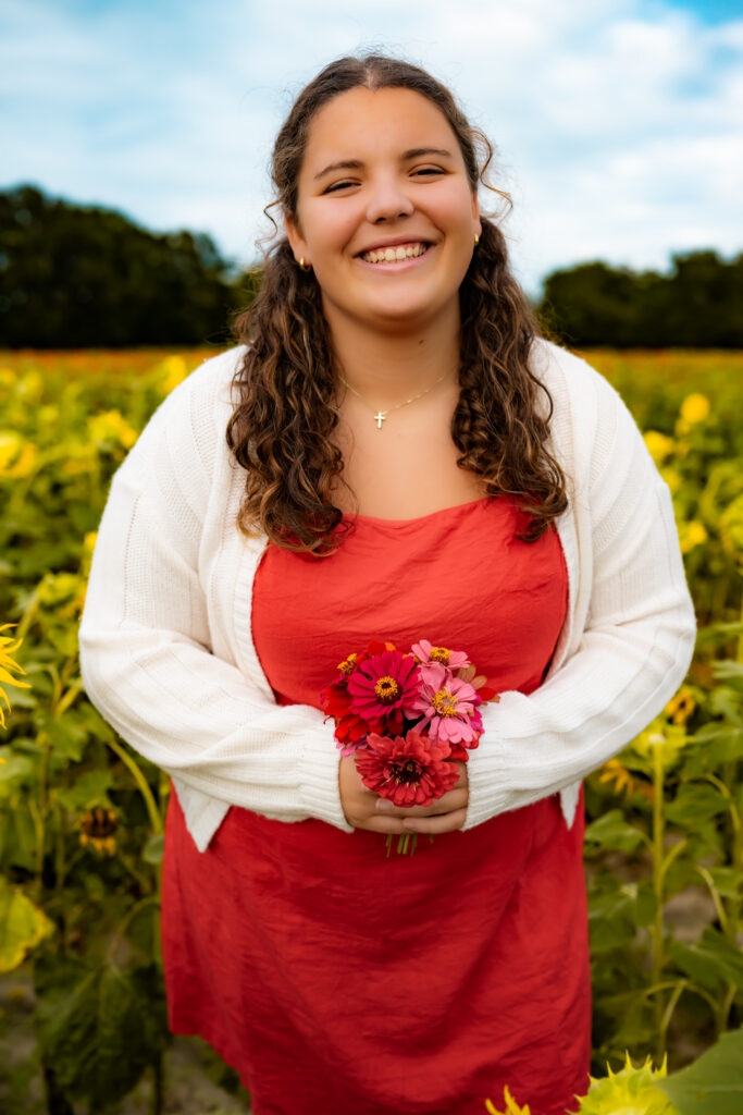 high school senior standing in a flower field with flowers, smiling.