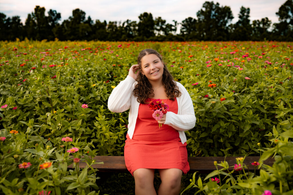 high school senior girl sitting in a flower field with flowers, smiling