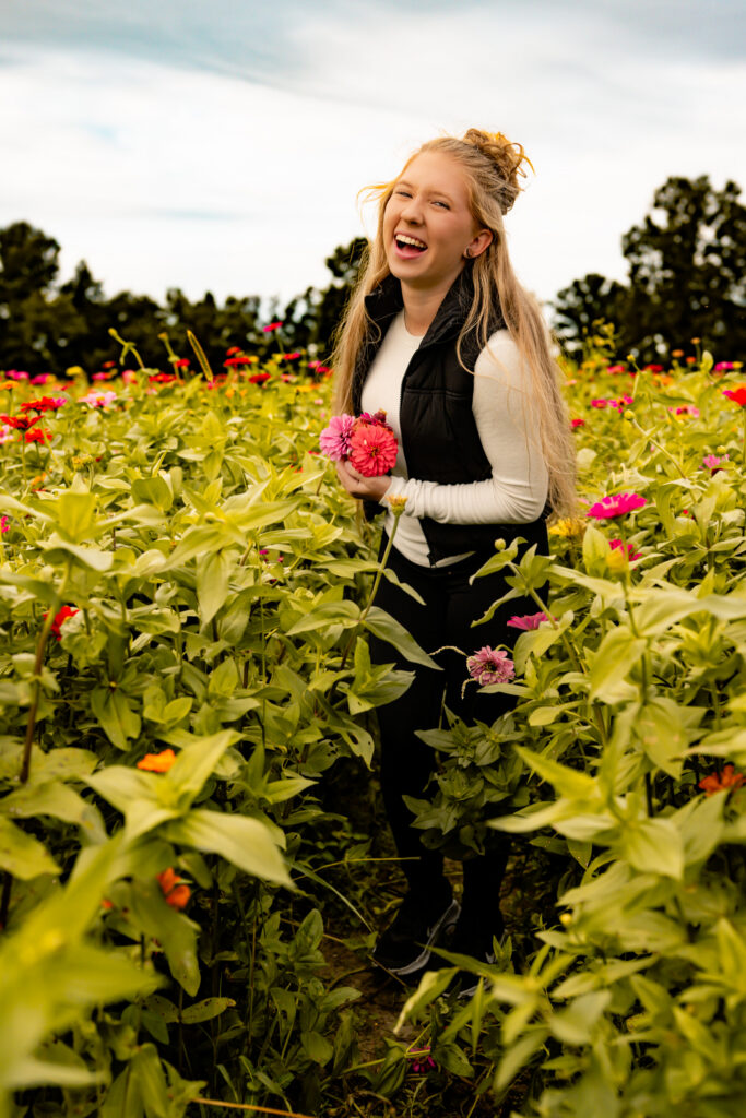 high school senior girl walking in a flower field laughing
