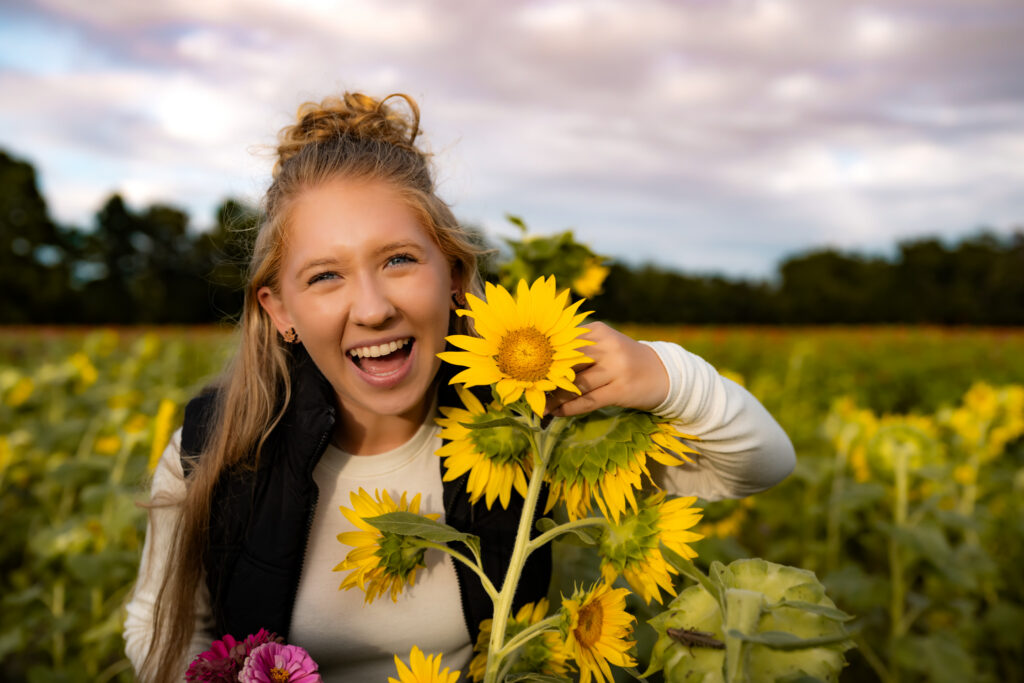 high school senior girl in a flower field, smiling with a sunflower