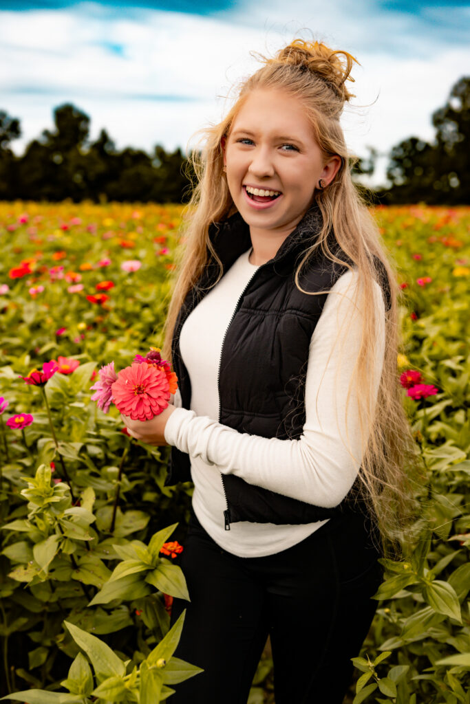 high school senior girl standing in a flower field with flowers, smiling