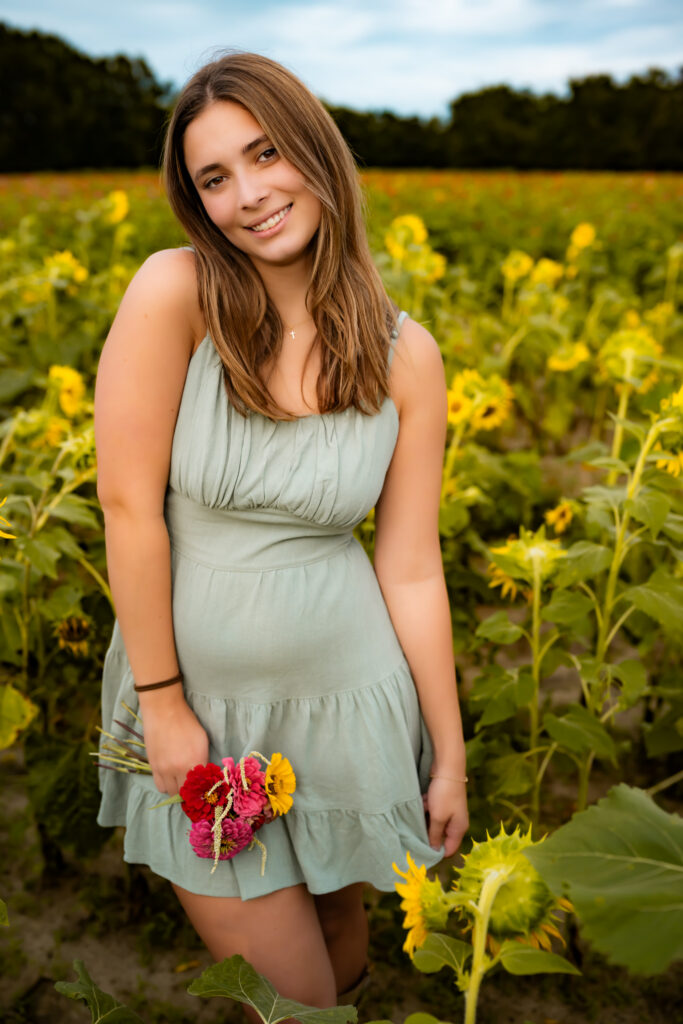 high school senior girl standing in a flower field with flowers, smiling.