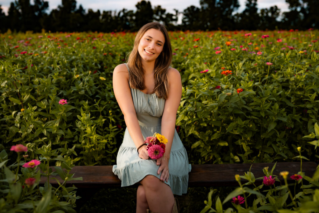 high school senior girl sitting in a flower field with flowers, smiling