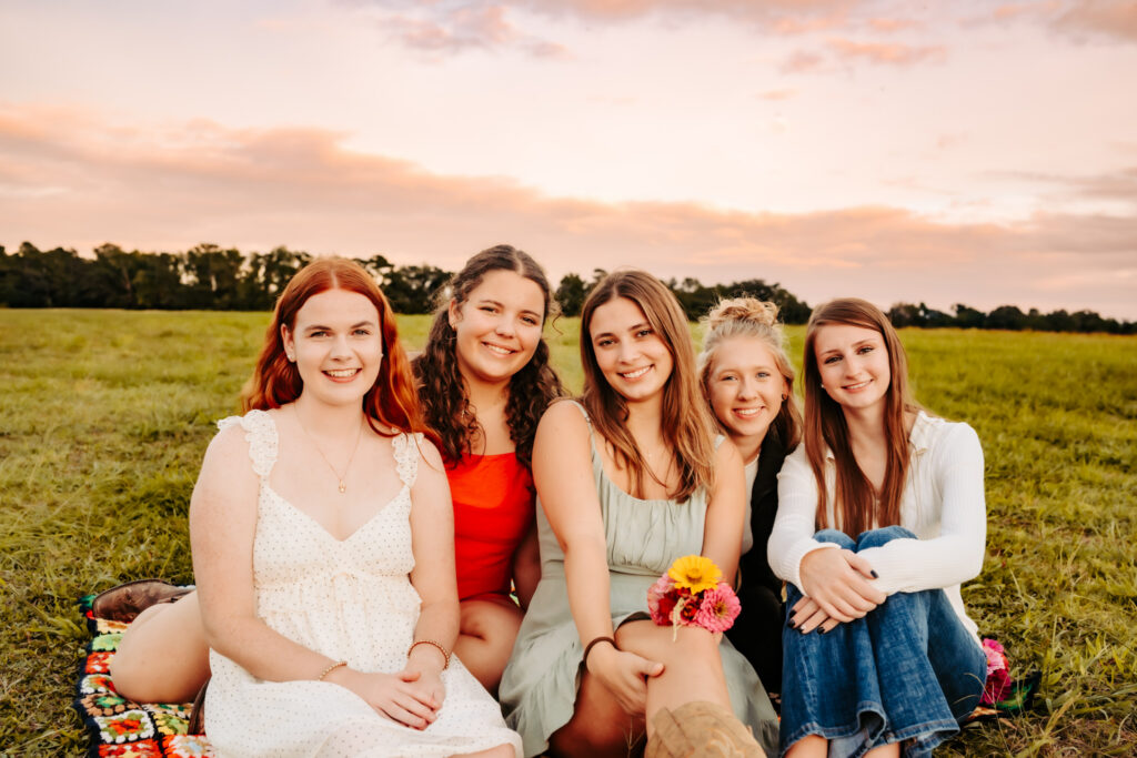 group of high school seniors sitting together in a field at sunset