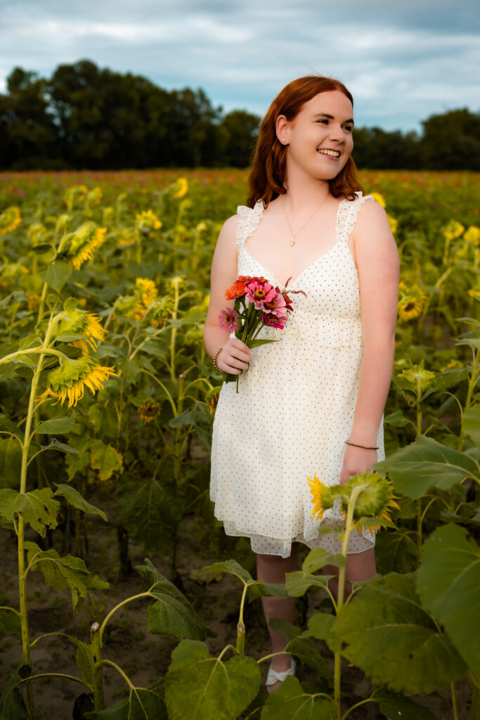 high school senior girl standing in a flower field with flowers, smiling