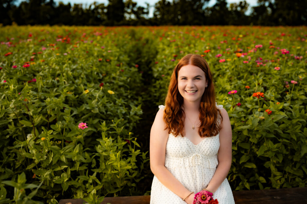 high school senior girl sitting in a flower field with flowers, smiling